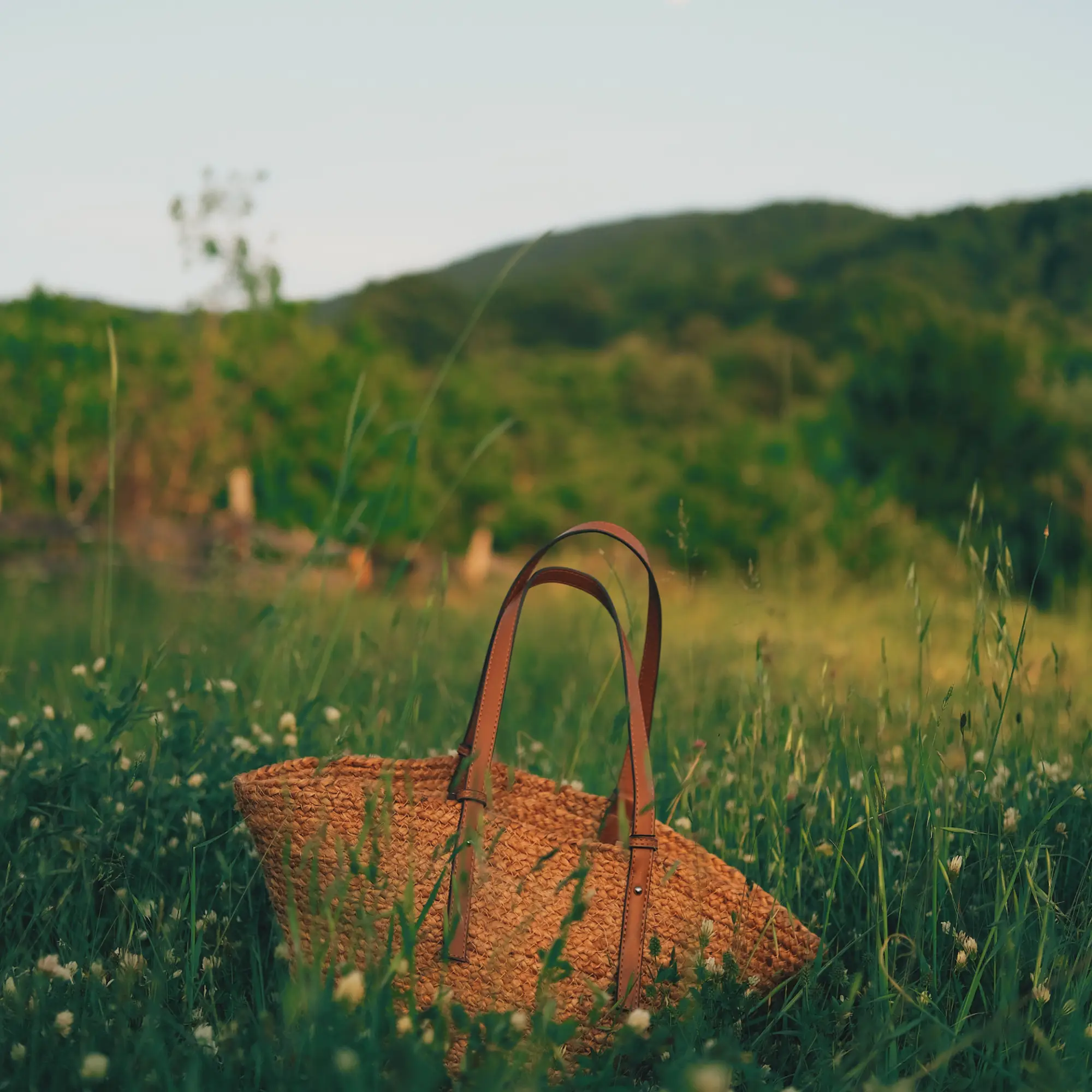 A bag made from straw sitting in a green field