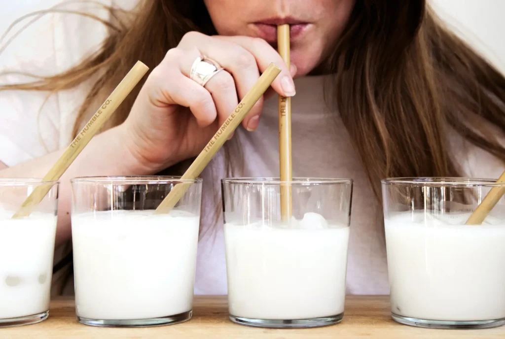 A woman sipping milk from a glass using a bamboo straw